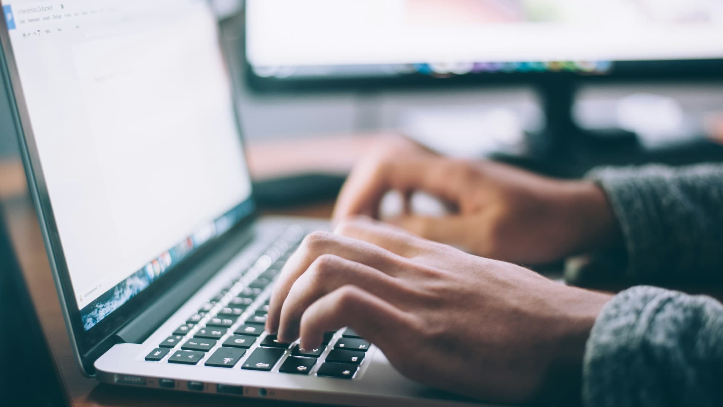 Person typing on a MacBook Pro at a white desk