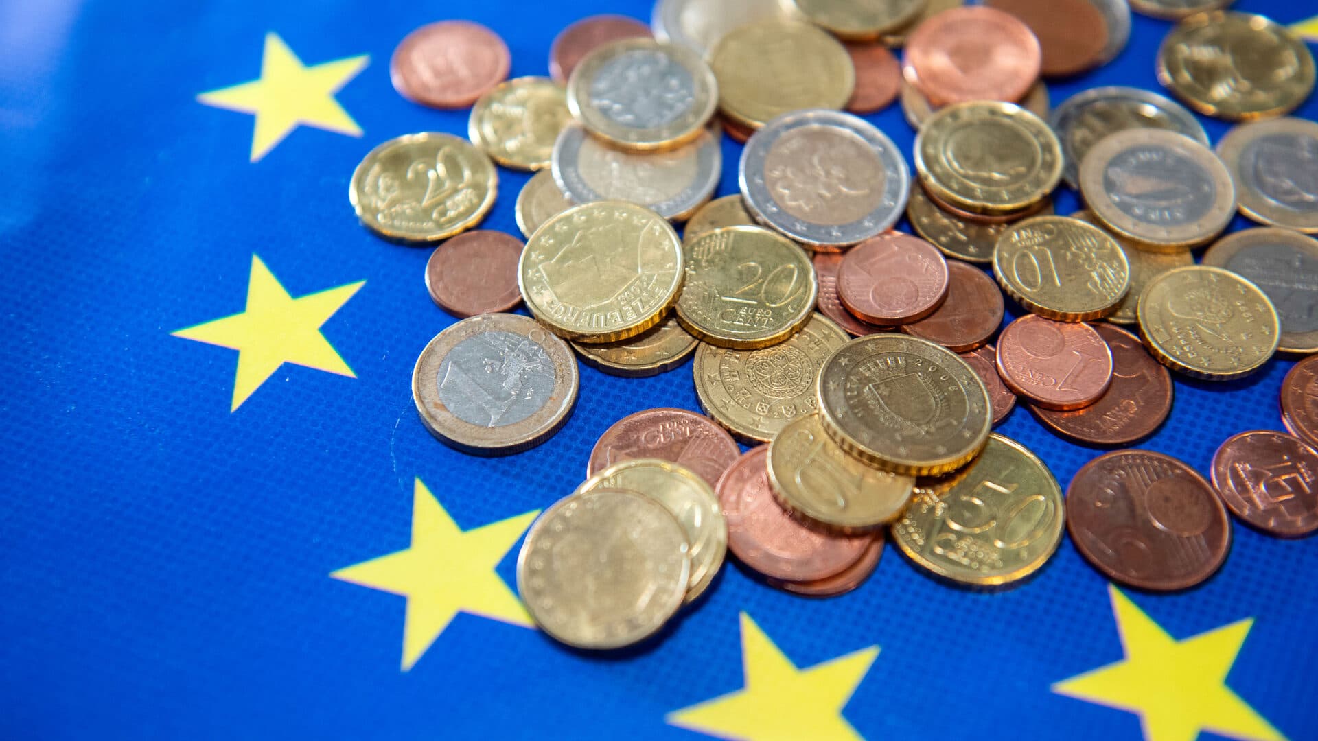 Euro coins scattered across a blue EU flag with yellow stars
