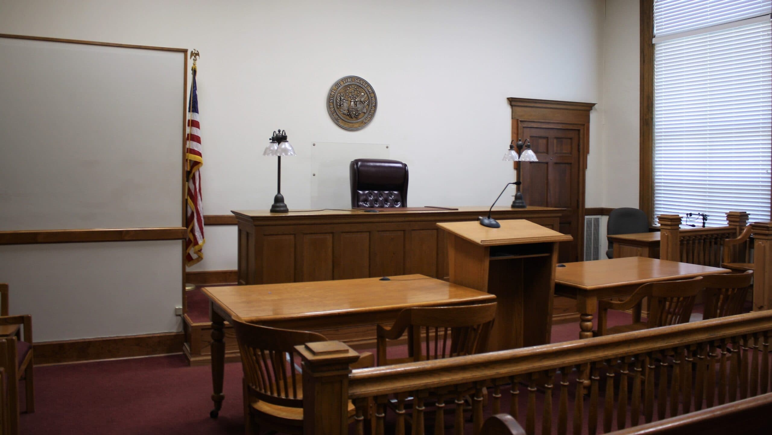 Empty US courtroom with a wooden judge's bench, counsel tables and an American flag