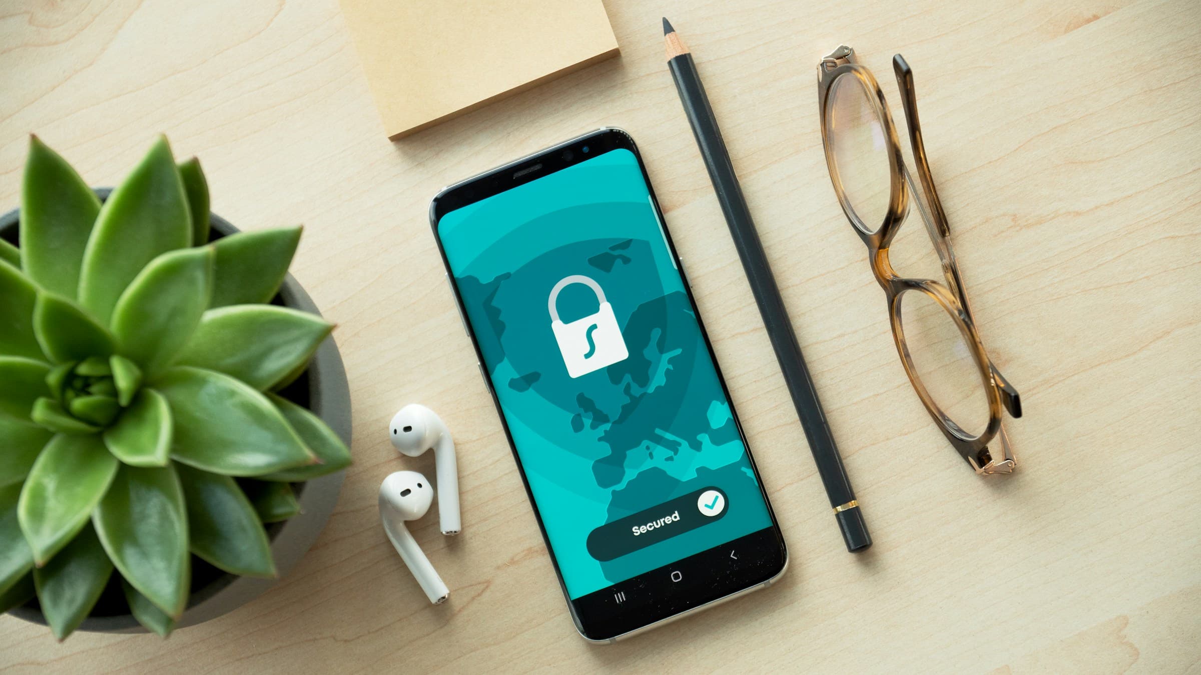 Smartphone showing a padlock security icon on a wooden desk next to a succulent, earphones and glasses