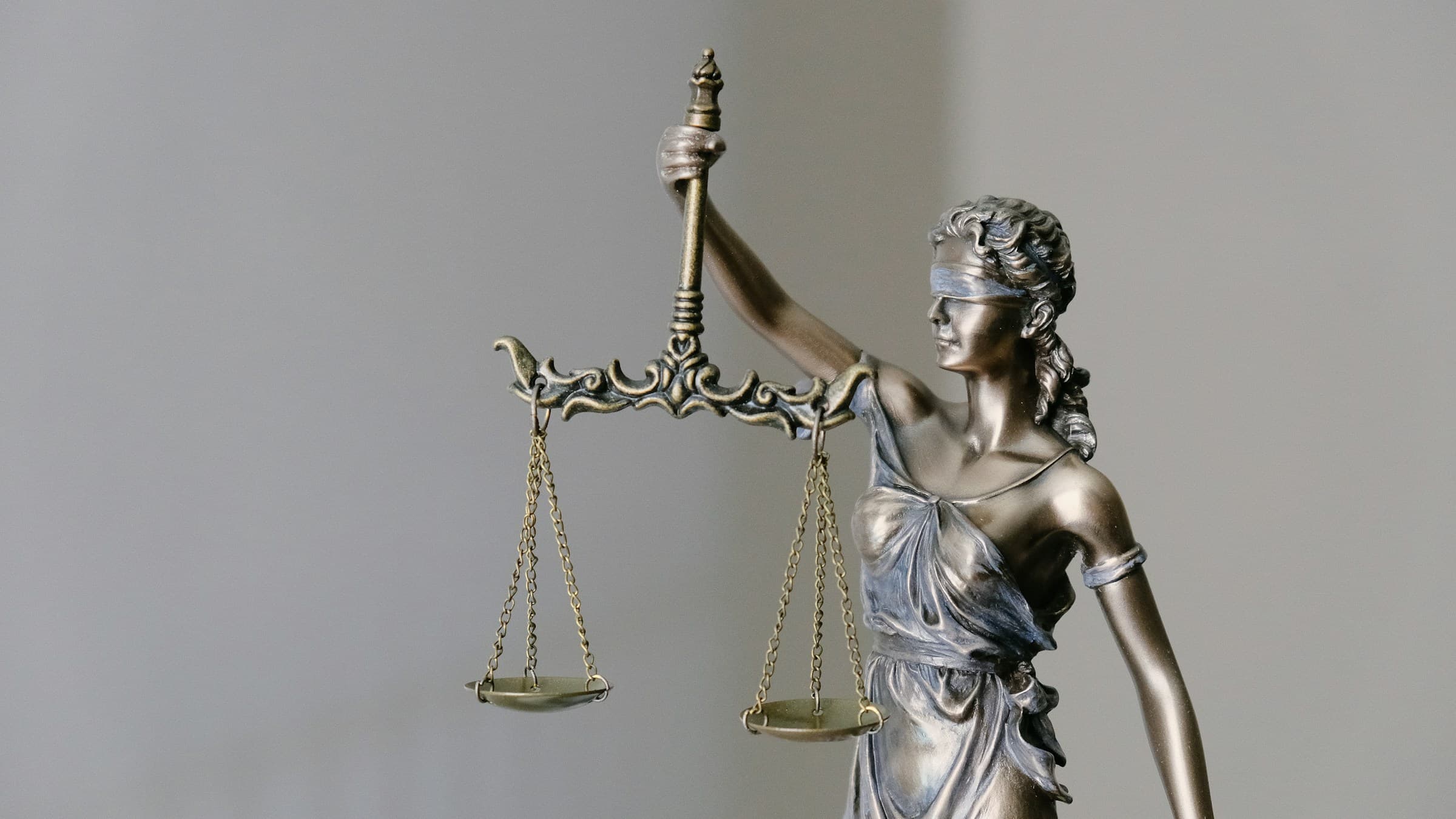 Bronze statue of Lady Justice holding scales against a grey background