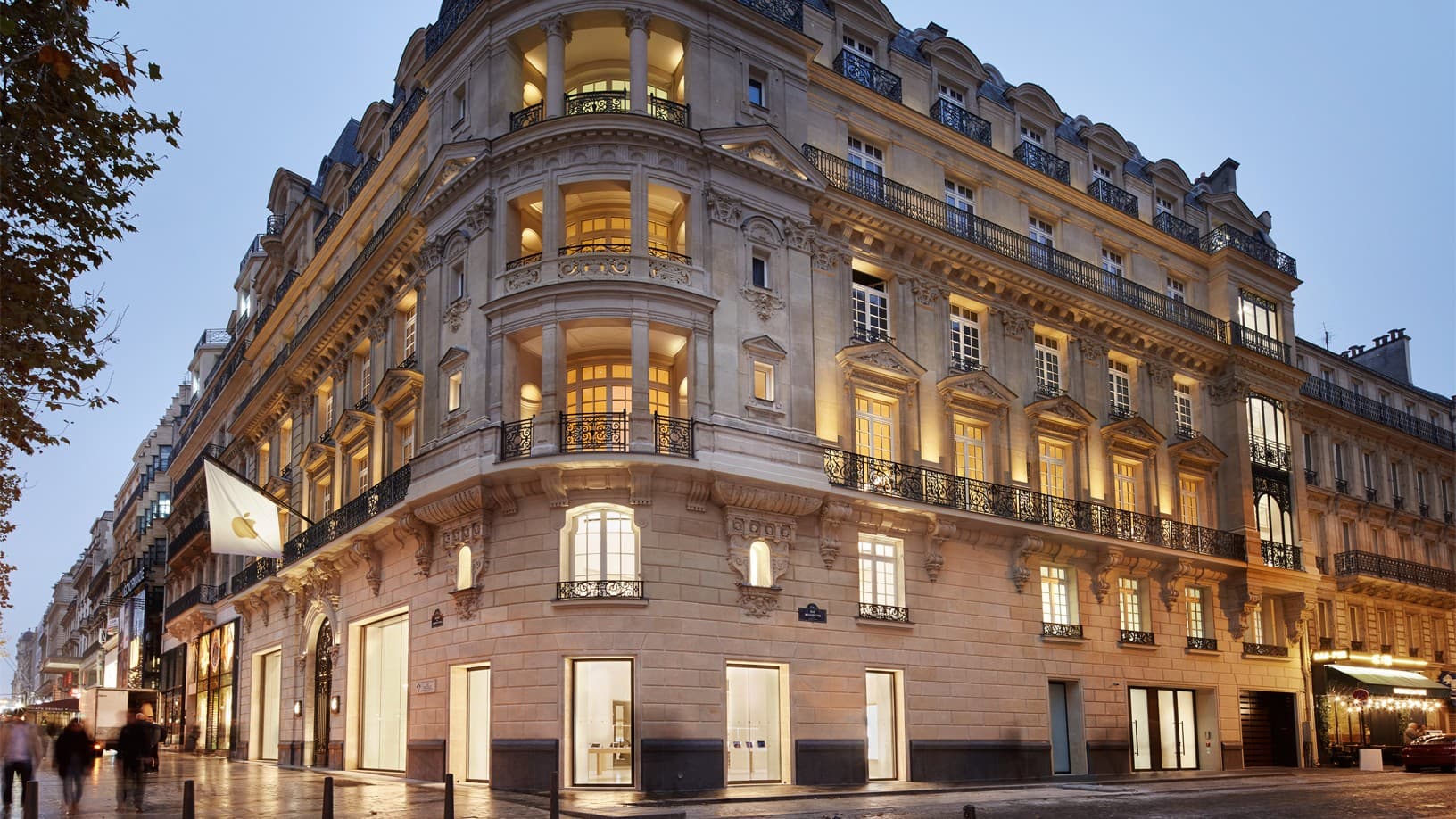 Exterior of the Apple Champs-Élysées store in Paris at dusk, with an Apple flag on the corner of the building