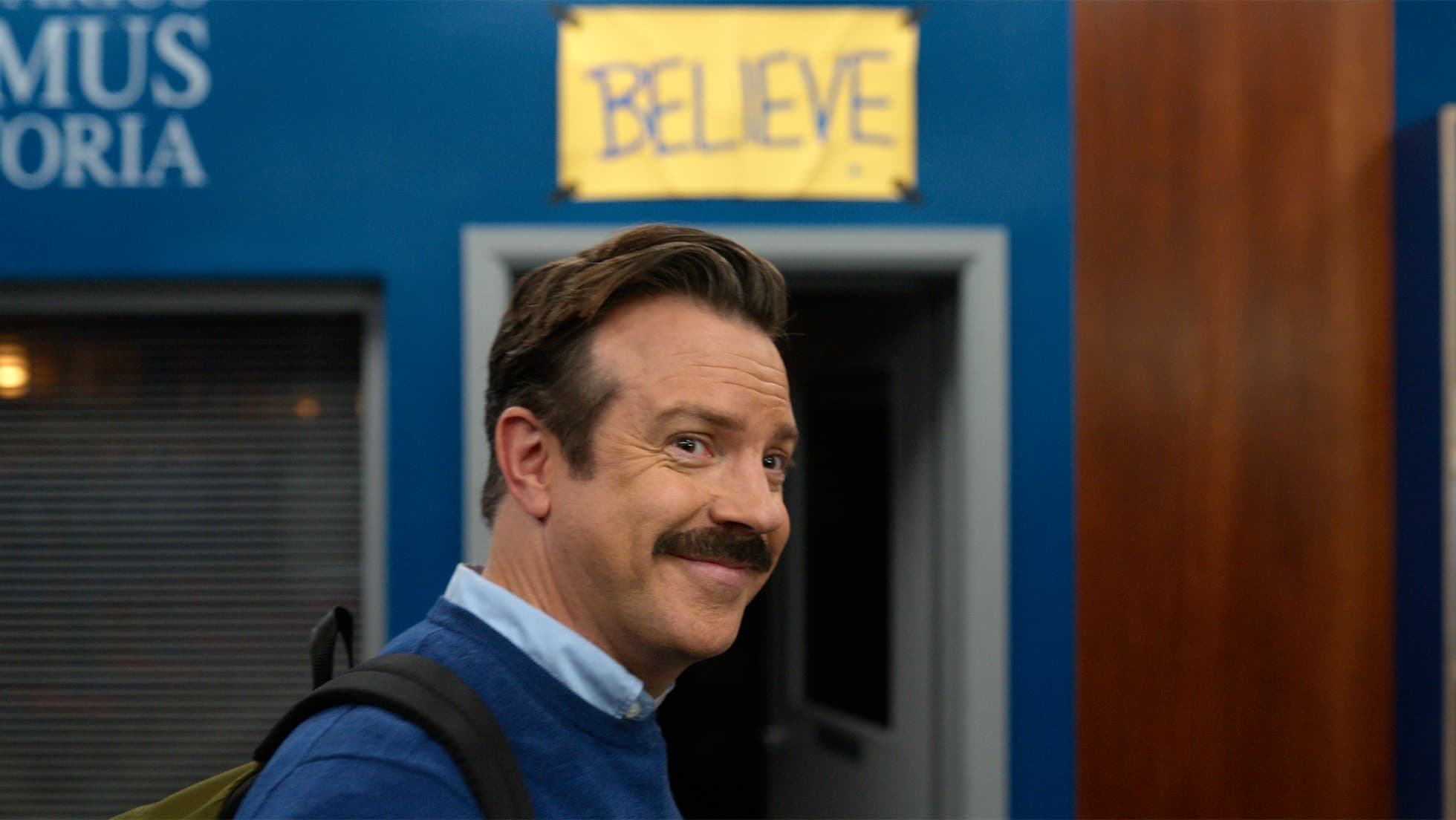 Jason Sudeikis as Ted Lasso smiling in front of the Believe sign in Ted Lasso season 4